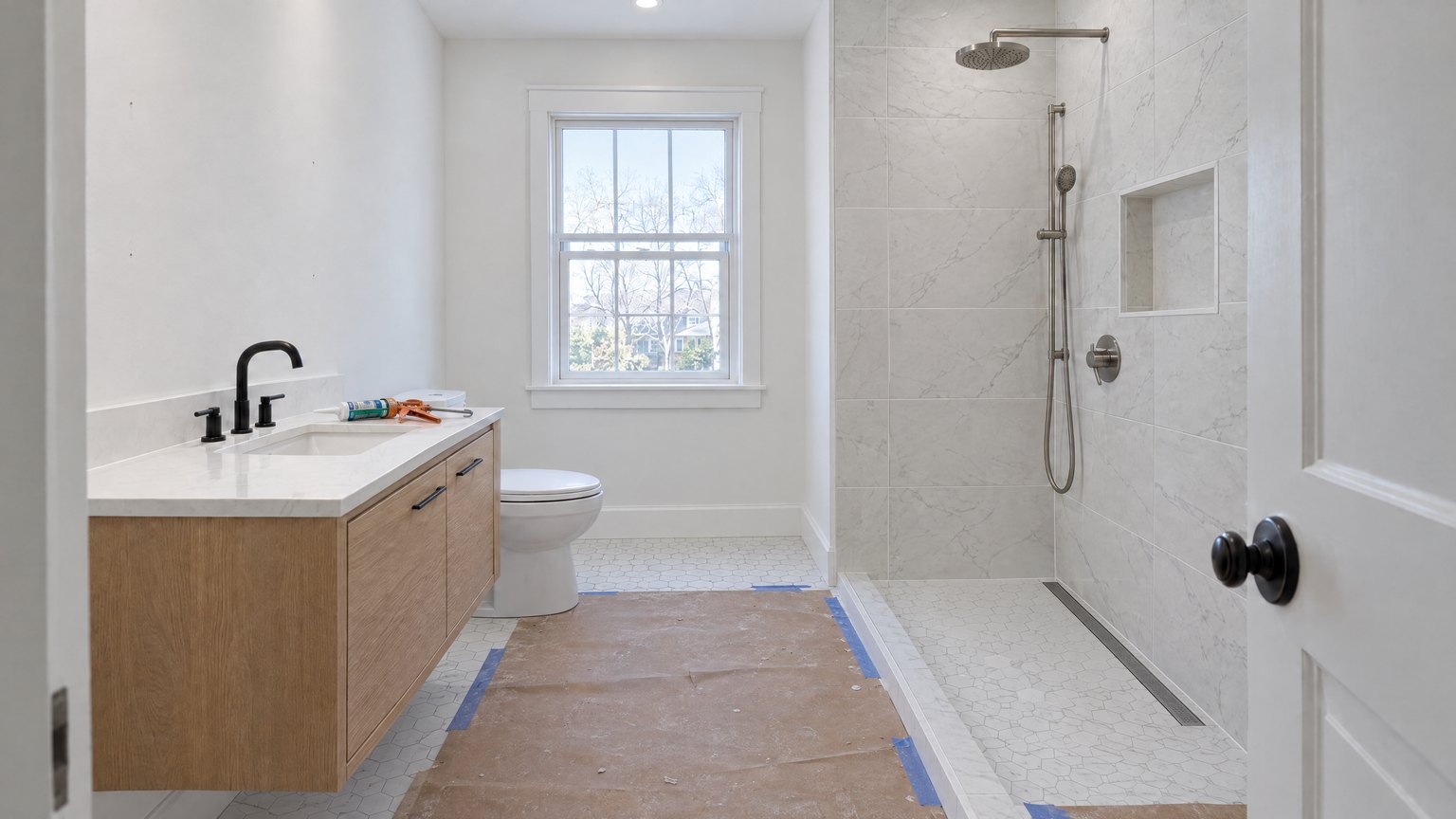 Fixtures: tile grouted, the floating oak vanity and quartz top hung, toilet set, rain head and handheld installed, no glass yet